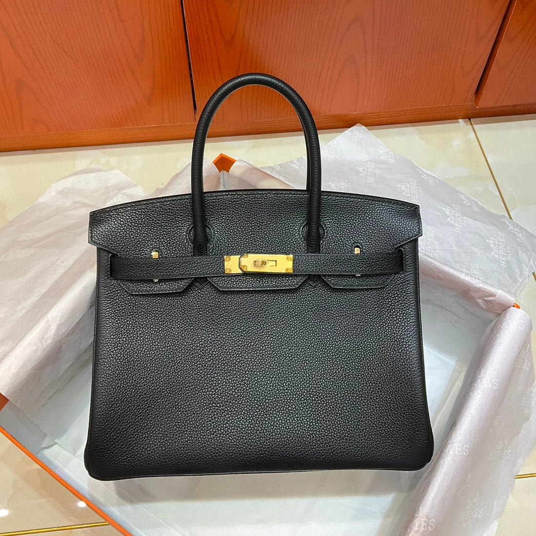 Deep Jet Black Uniform Pebbled Grain Medium Folded Structured Hand Tote With Seamless Matching Stitching, Lustrous Golden Twist Lock Hardware And Coordinating Suspended Textured Tag Striped Metal Padlock Charm